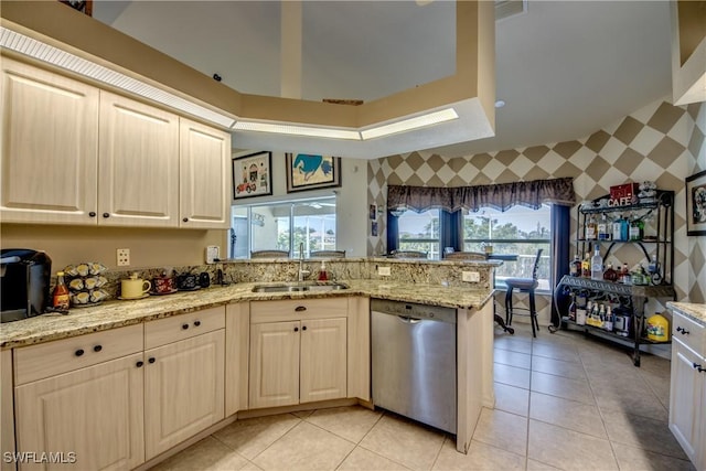 kitchen featuring dishwasher, a raised ceiling, light stone counters, kitchen peninsula, and light tile patterned floors