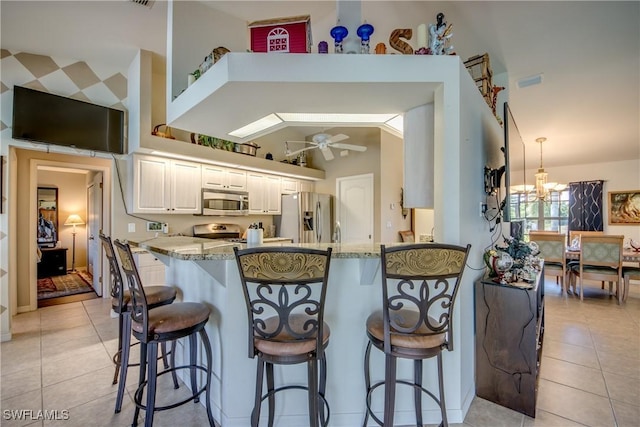 kitchen with appliances with stainless steel finishes, light stone counters, ceiling fan with notable chandelier, white cabinets, and light tile patterned flooring