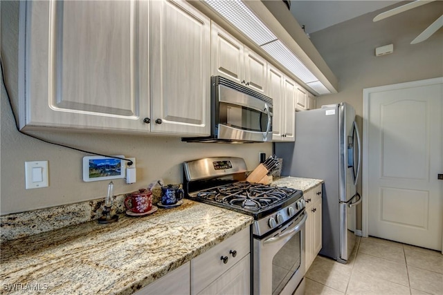 kitchen featuring ceiling fan, light stone counters, light tile patterned floors, and appliances with stainless steel finishes