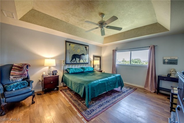 bedroom with wood-type flooring, a raised ceiling, and ceiling fan