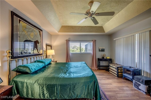 bedroom with a raised ceiling, ceiling fan, wood-type flooring, and a textured ceiling