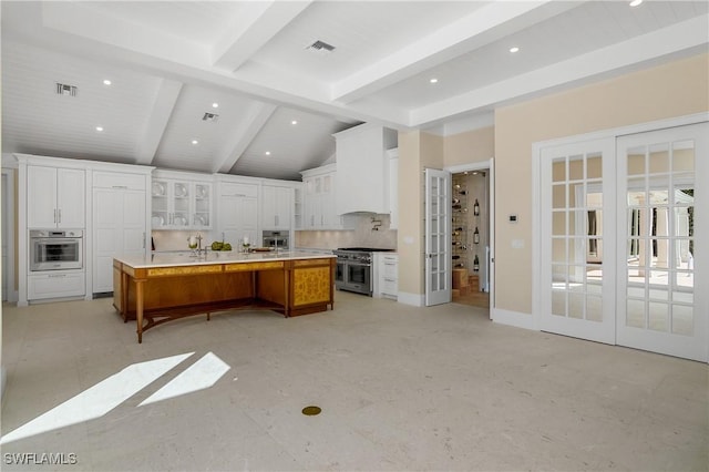 kitchen with french doors, a spacious island, beam ceiling, white cabinetry, and stainless steel appliances