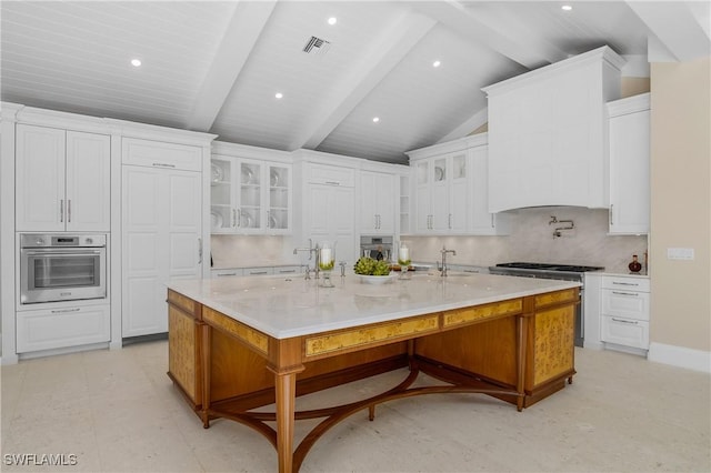 kitchen with light stone counters, stainless steel appliances, a large island with sink, vaulted ceiling with beams, and white cabinetry