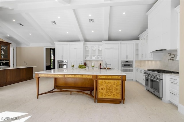 kitchen featuring a large island with sink, white cabinetry, and range with two ovens