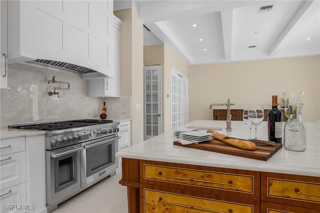 kitchen featuring custom range hood, backsplash, white cabinetry, and range with two ovens