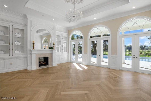 unfurnished living room with plenty of natural light, ornamental molding, a fireplace, and french doors