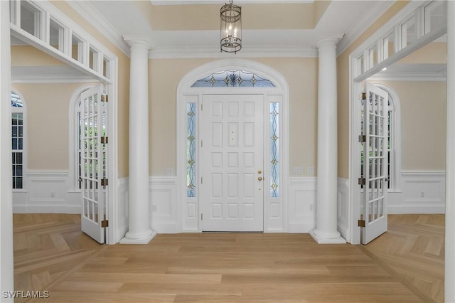 entryway with light parquet flooring, an inviting chandelier, ornamental molding, and ornate columns