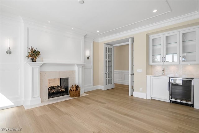 unfurnished living room featuring a tiled fireplace, ornamental molding, beverage cooler, and wet bar