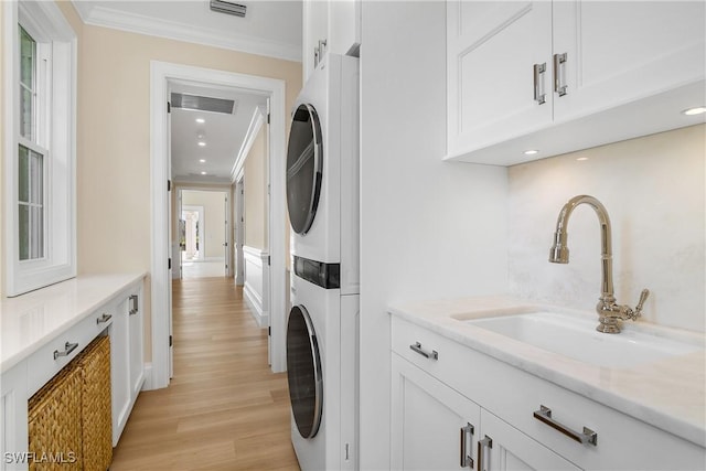 laundry area featuring crown molding, stacked washing maching and dryer, sink, and light hardwood / wood-style flooring