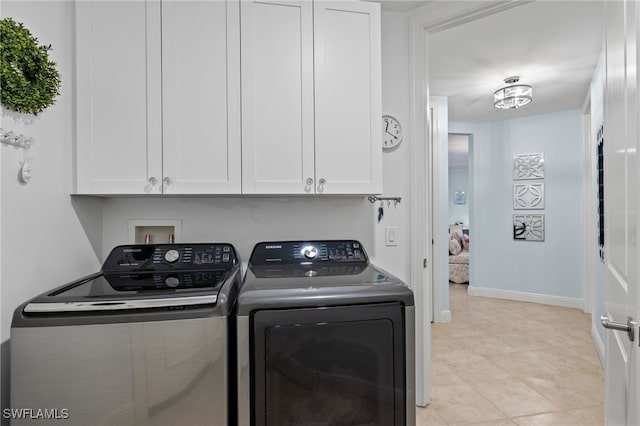 laundry area featuring washing machine and clothes dryer, light tile patterned floors, and cabinets