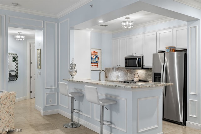 kitchen featuring kitchen peninsula, appliances with stainless steel finishes, light stone counters, white cabinetry, and a breakfast bar area