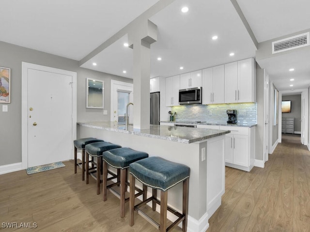 kitchen featuring light stone counters, light hardwood / wood-style floors, a kitchen bar, white cabinets, and appliances with stainless steel finishes