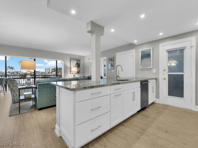 kitchen featuring white cabinets, kitchen peninsula, dark stone counters, sink, and light hardwood / wood-style flooring