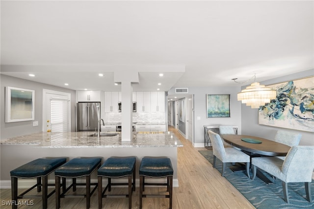 kitchen with sink, white cabinetry, decorative backsplash, light stone countertops, and high end fridge