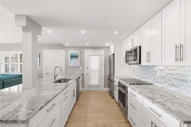 kitchen with light stone counters, stainless steel appliances, tasteful backsplash, white cabinetry, and sink