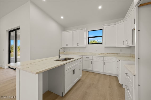 kitchen featuring a center island with sink, sink, white cabinetry, light wood-type flooring, and light stone counters