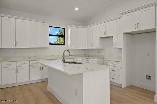 kitchen with light stone countertops, white cabinets, lofted ceiling, sink, and a kitchen island with sink