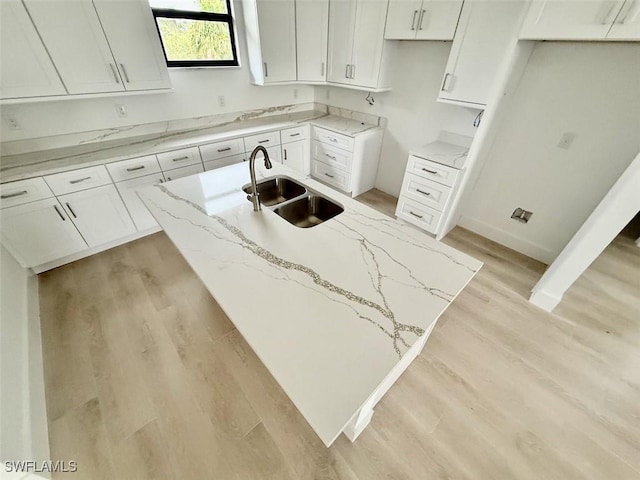 kitchen with light stone counters, sink, white cabinetry, and light hardwood / wood-style flooring