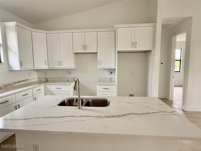 kitchen featuring vaulted ceiling, light stone countertops, a center island with sink, and sink