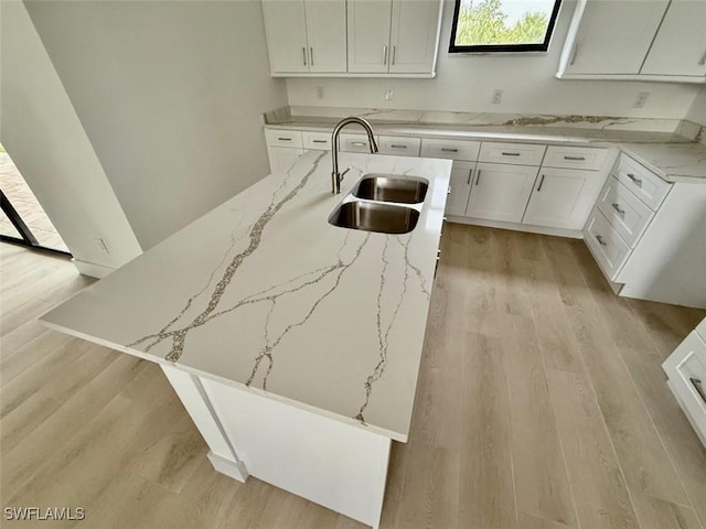 kitchen with light hardwood / wood-style floors, sink, an island with sink, white cabinets, and light stone counters