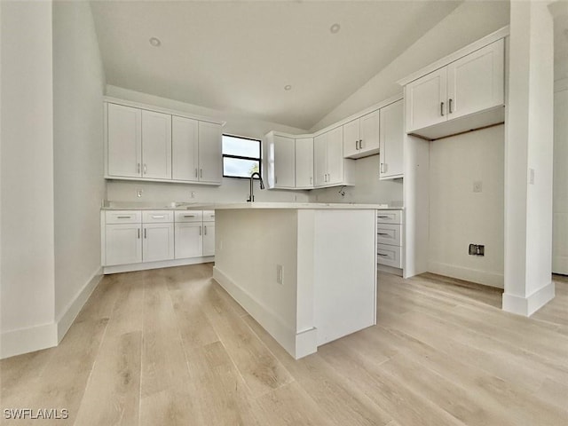 kitchen with white cabinets, vaulted ceiling, light hardwood / wood-style flooring, and a kitchen island