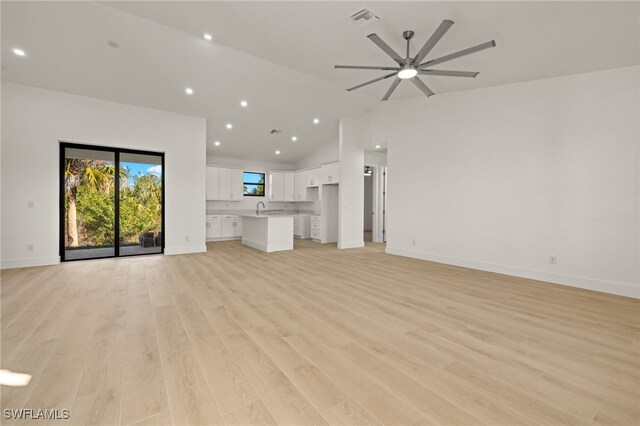 unfurnished living room with ceiling fan, light wood-type flooring, sink, and high vaulted ceiling