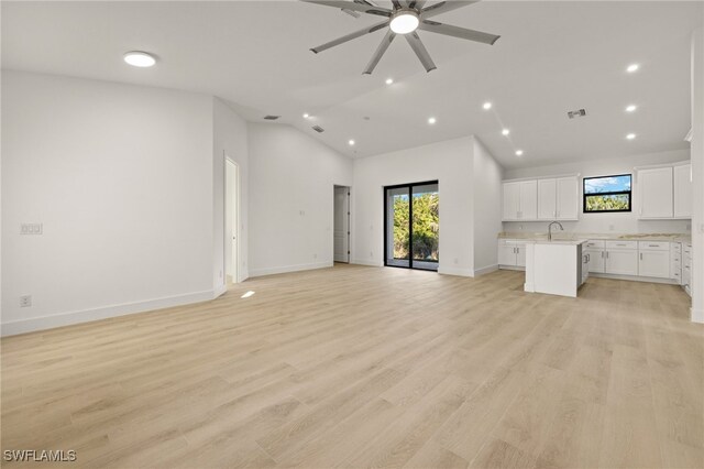 unfurnished living room with ceiling fan, light hardwood / wood-style floors, high vaulted ceiling, and sink