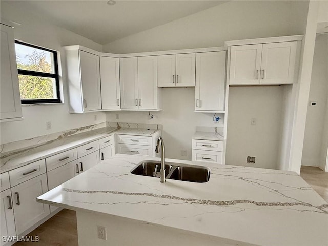 kitchen featuring lofted ceiling, white cabinets, light stone countertops, and sink