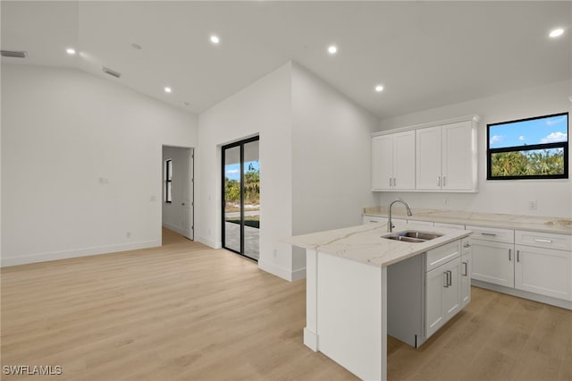 kitchen with light stone countertops, sink, white cabinetry, and a center island with sink