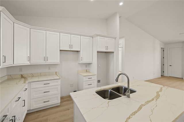 kitchen featuring light hardwood / wood-style floors, vaulted ceiling, white cabinets, light stone counters, and sink