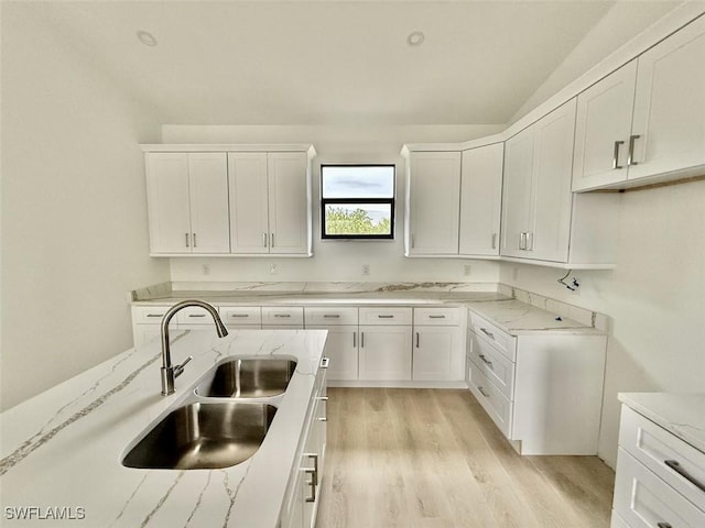 kitchen featuring light stone countertops, white cabinetry, and sink