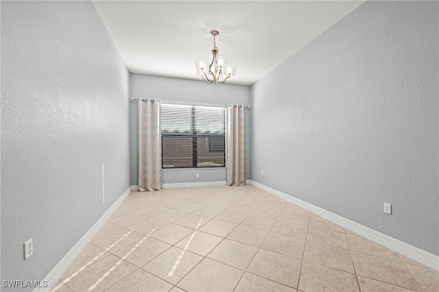 tiled spare room with an inviting chandelier