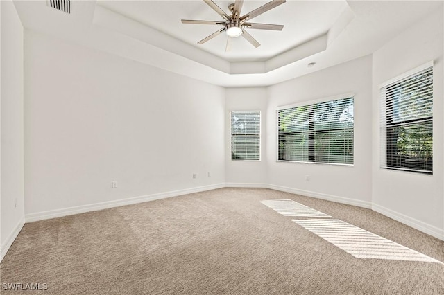 carpeted empty room featuring ceiling fan and a raised ceiling