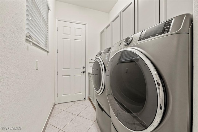 clothes washing area featuring light tile patterned flooring, cabinets, and separate washer and dryer