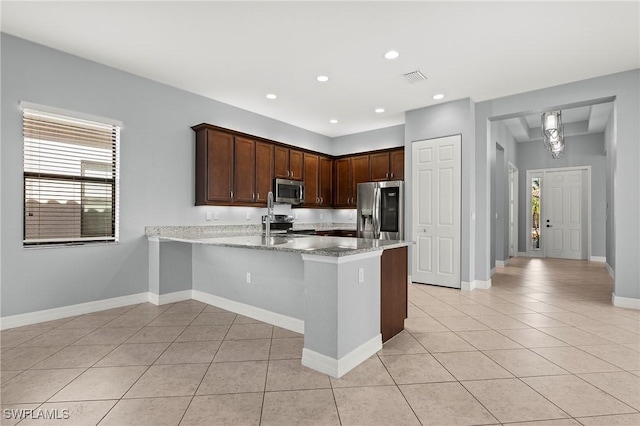 kitchen with light stone countertops, appliances with stainless steel finishes, dark brown cabinets, light tile patterned flooring, and kitchen peninsula