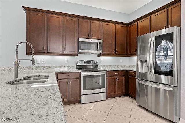 kitchen featuring light tile patterned flooring, appliances with stainless steel finishes, light stone counters, and sink