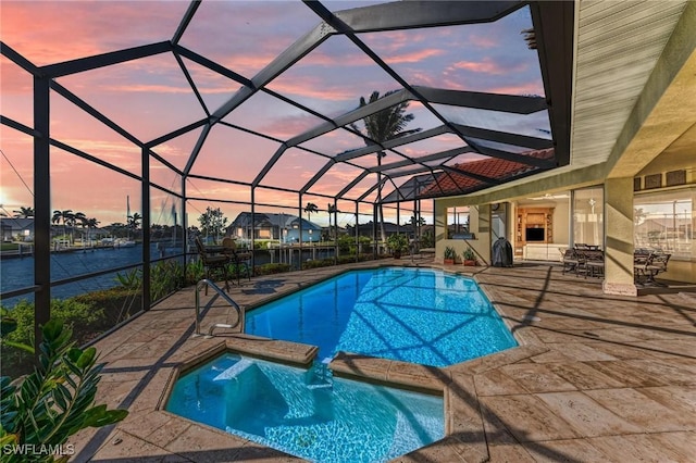 pool at dusk with glass enclosure, a water view, and a patio