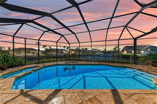 pool at dusk with glass enclosure, a patio area, a water view, and an in ground hot tub