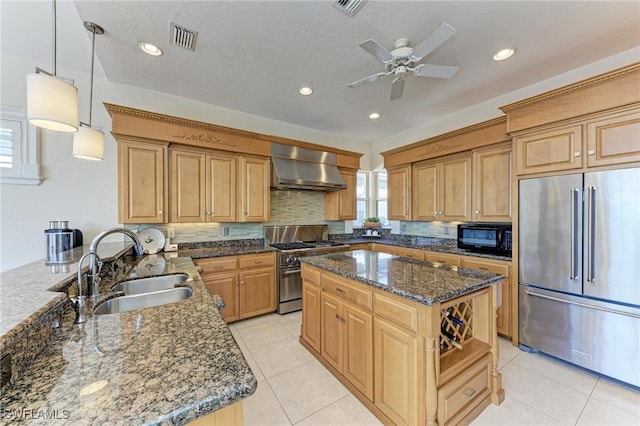 kitchen with wall chimney exhaust hood, sink, high quality appliances, dark stone countertops, and hanging light fixtures