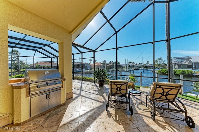 view of patio / terrace with a lanai, grilling area, a water view, and exterior kitchen