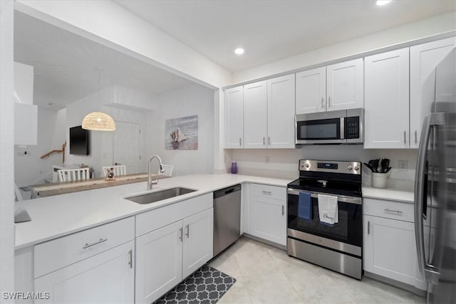 kitchen with stainless steel appliances, kitchen peninsula, sink, white cabinetry, and decorative light fixtures