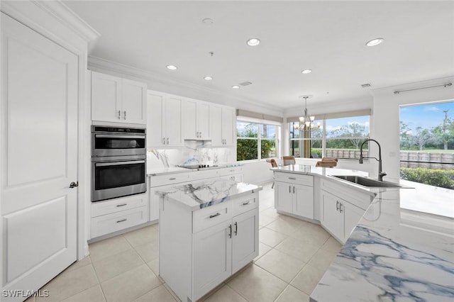 kitchen featuring sink, double oven, black electric stovetop, a center island with sink, and decorative light fixtures