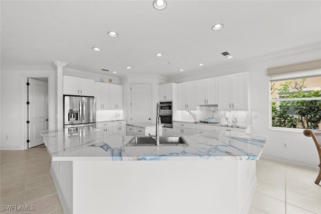 kitchen featuring light tile patterned flooring, a sink, appliances with stainless steel finishes, a large island with sink, and crown molding