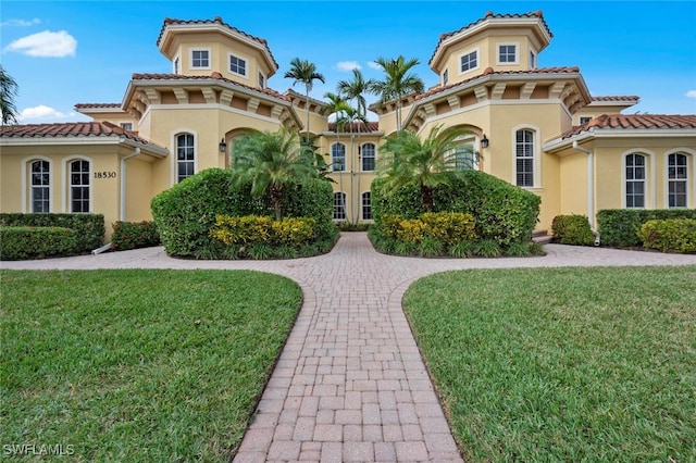 mediterranean / spanish house with a tiled roof, a front yard, and stucco siding