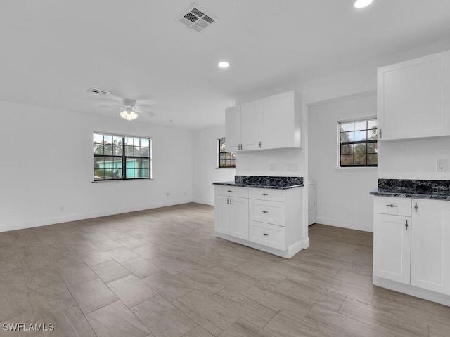 kitchen with ceiling fan, a healthy amount of sunlight, white cabinetry, and dark stone counters