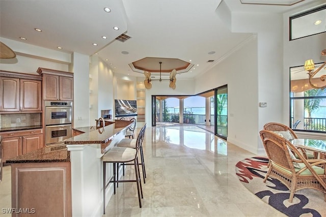 kitchen with a center island, a kitchen bar, crown molding, double oven, and dark stone countertops