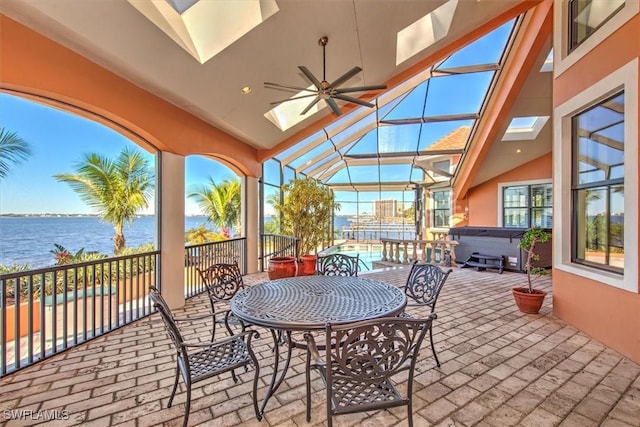 view of patio / terrace featuring glass enclosure, ceiling fan, a hot tub, and a water view