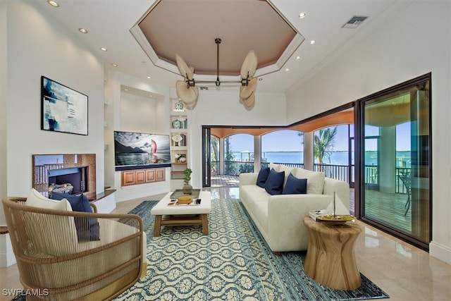 living room featuring a towering ceiling, a raised ceiling, built in features, and crown molding