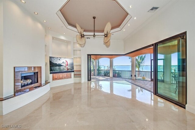 unfurnished living room with built in features, a tray ceiling, and crown molding