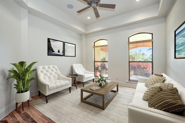 living area with a raised ceiling, hardwood / wood-style floors, and ceiling fan